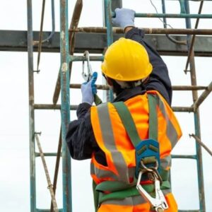 Worker wearing an orange high-visibility vest and a safety helmet, positioned on a scaffold ladder, performing tasks at height on a construction site